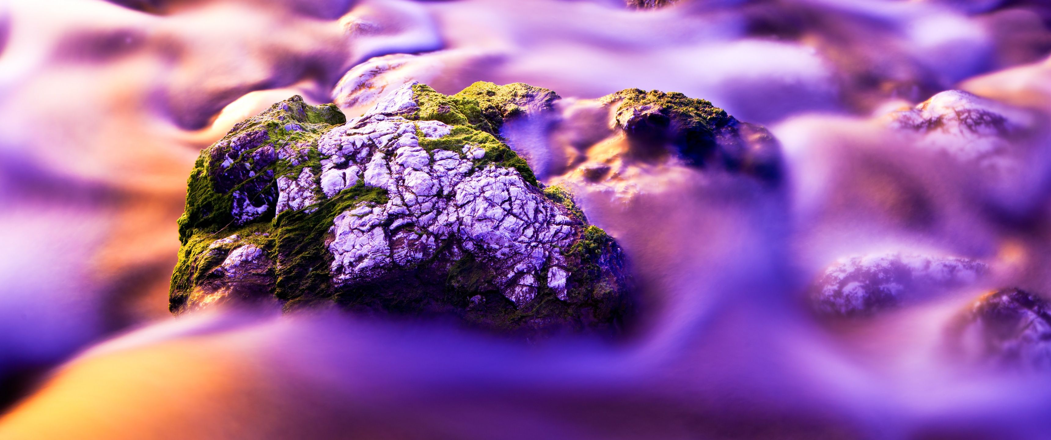 A close up of a rock covered in moss, surrounded by a blur of water. - 3440x1440, purple